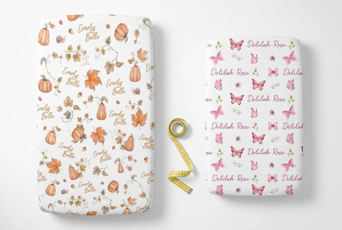 Two personalized crib sheets shown flat side by side, a standard 28 by 52 inch and a mini 24 by 38 inch, with a tape measure