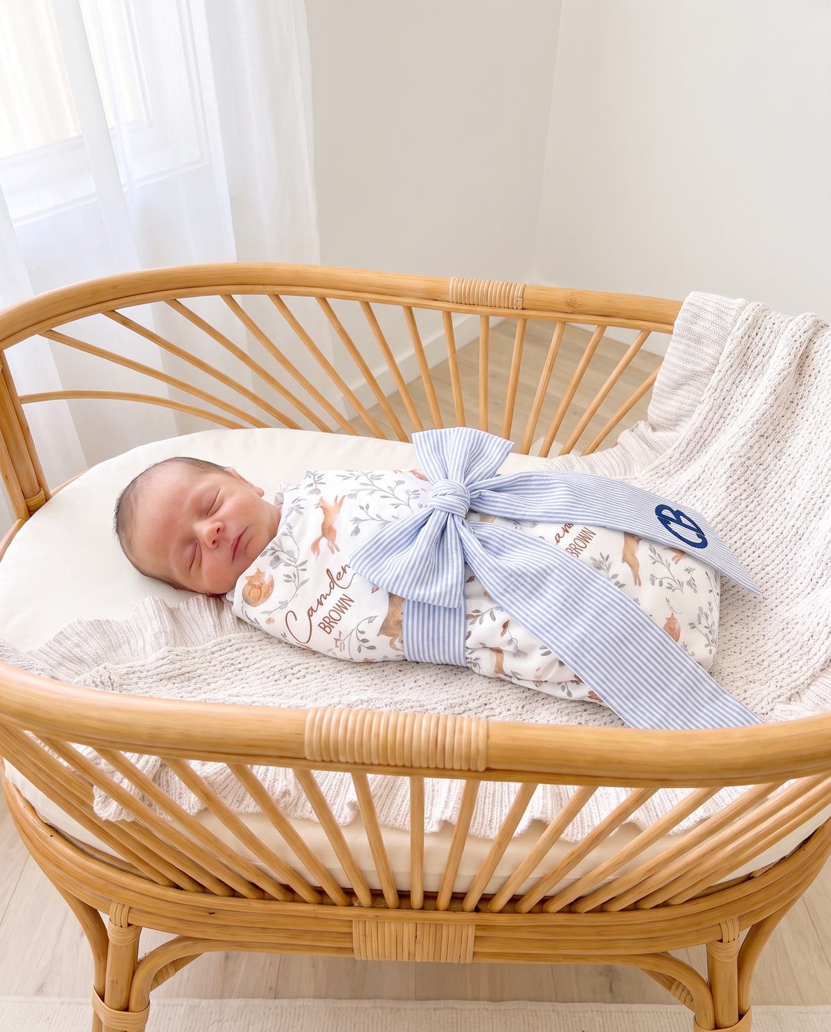Striped blue bow sash draped over a swaddled baby in a rattan crib