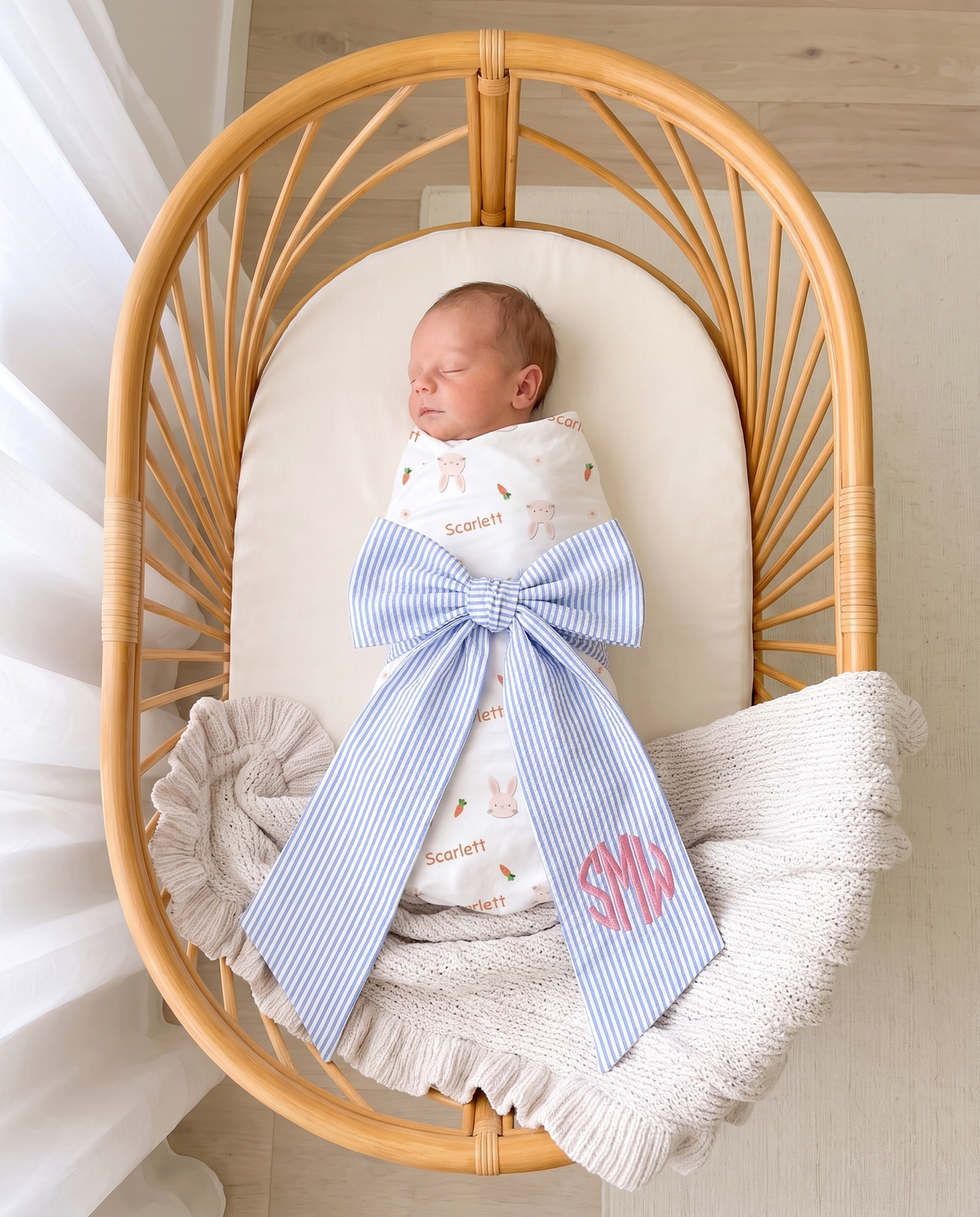 Striped blue bow sash with pink monogram on a swaddled newborn in a bassinet