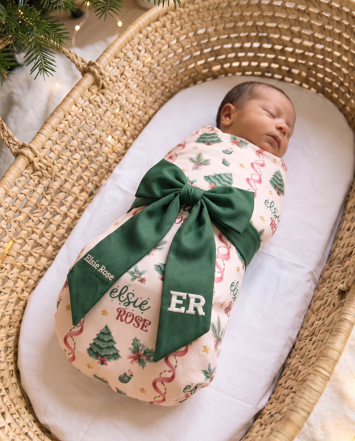 Swaddled newborn in a woven basket with the green bow sash and white name embroidery