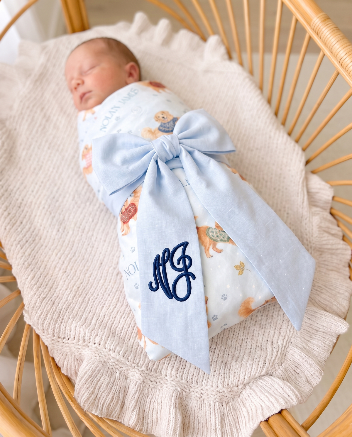 Sleeping baby wrapped in a swaddle with the light blue monogrammed bow sash tied across