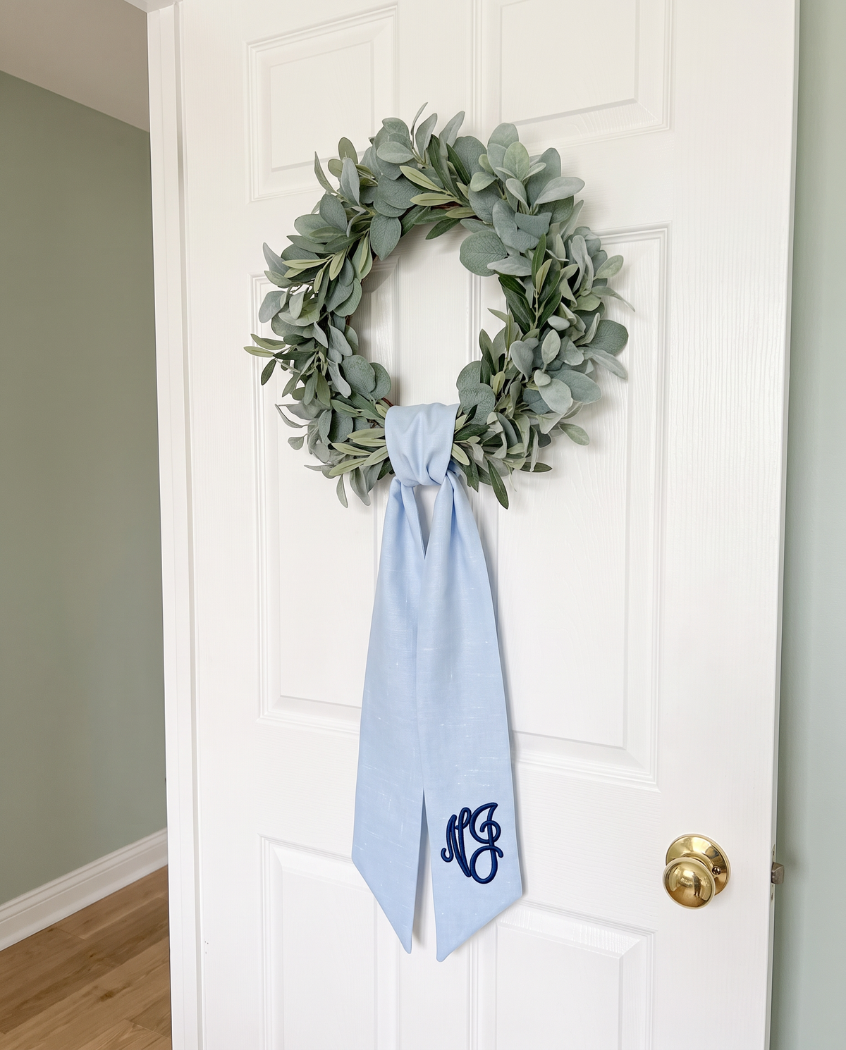 Light blue bow sash hanging on a nursery door below a eucalyptus wreath