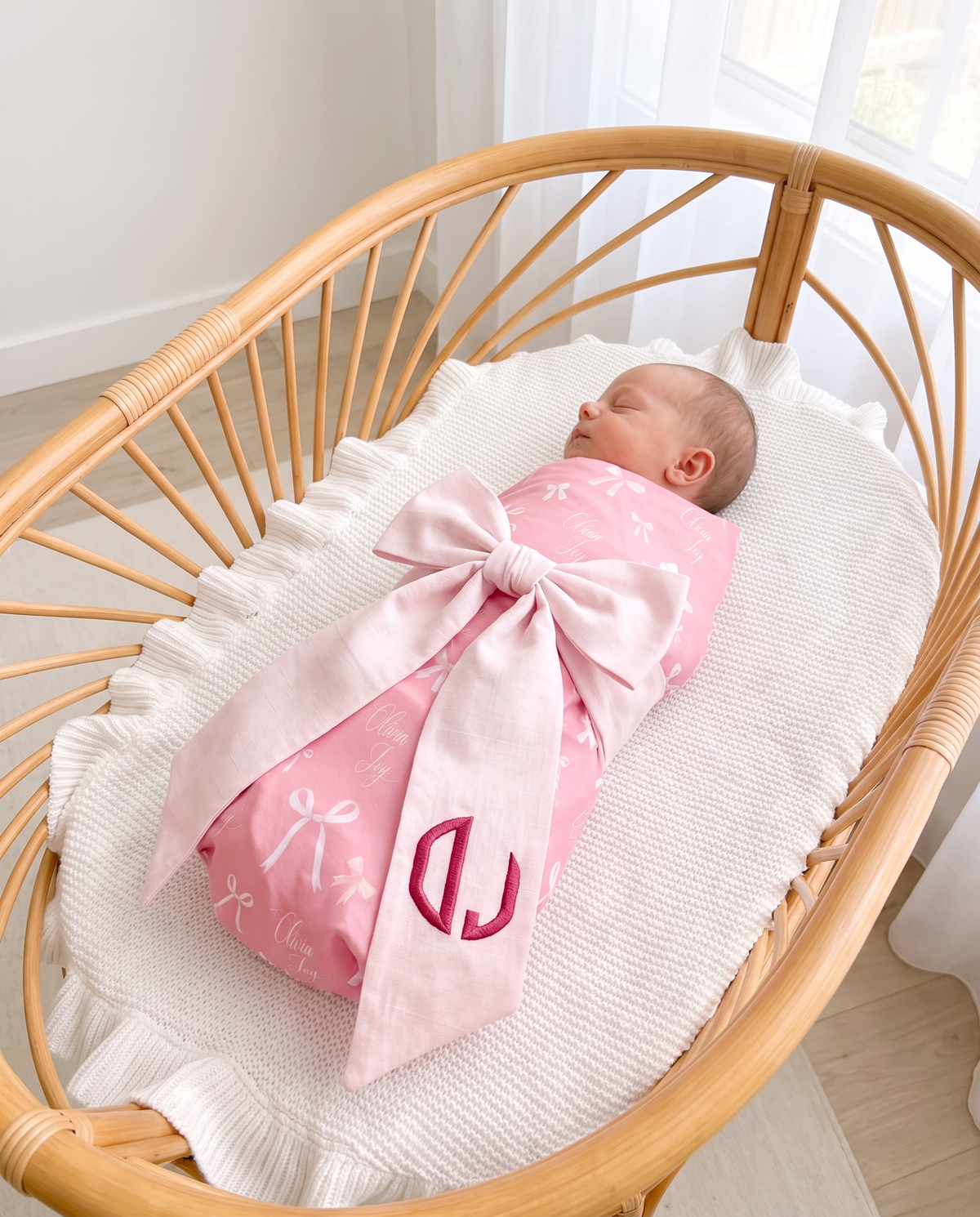 Newborn in pink swaddle with the monogrammed light pink bow sash lying across