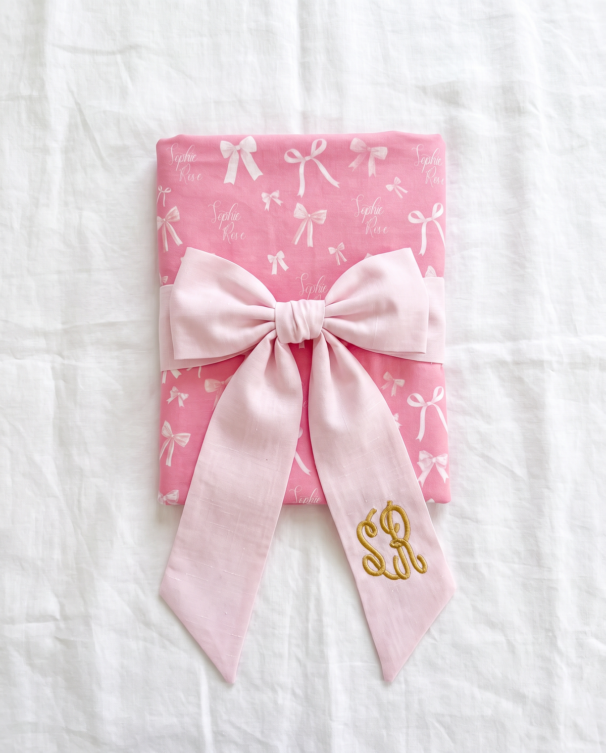 Light pink bow sash tied around a folded pink swaddle as a baby gift