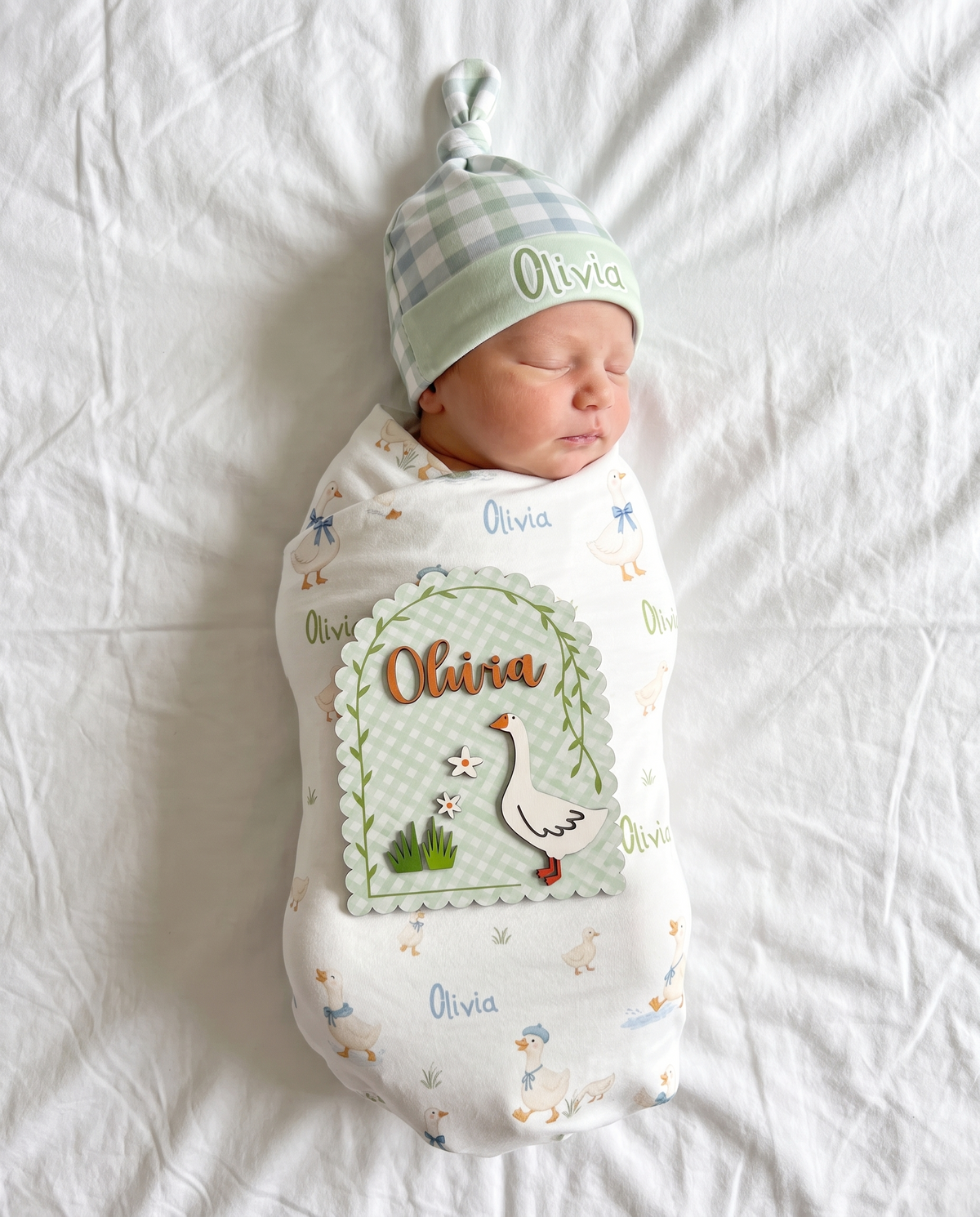 Little Goose wood announcement sign shown from above with a matching swaddle and knotted hat