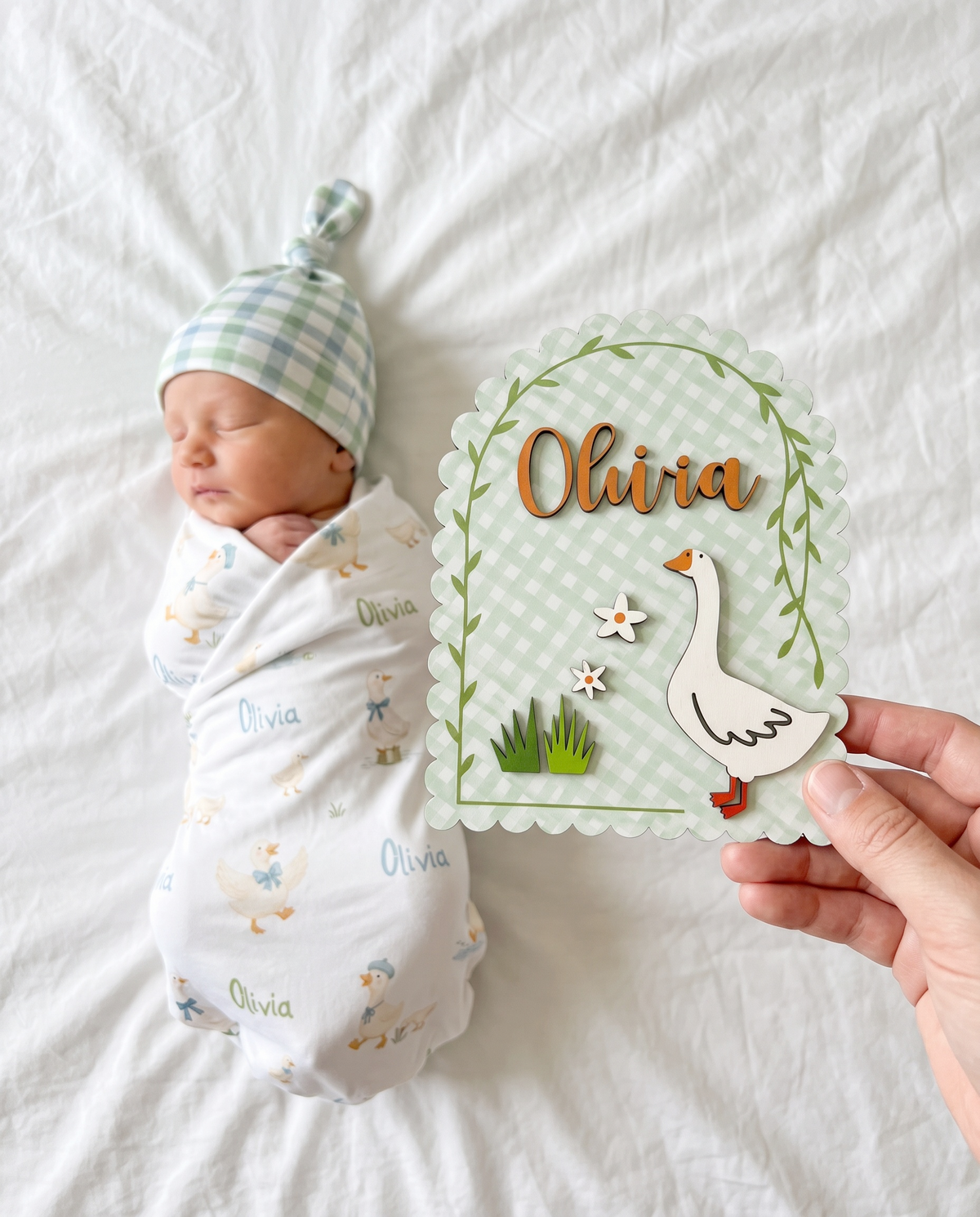 Hands holding the Little Goose personalized wood announcement sign with a wooden goose on sage gingham