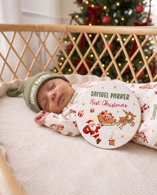 Newborn sleeping beside the personalized First Christmas name sign in a rattan bassinet