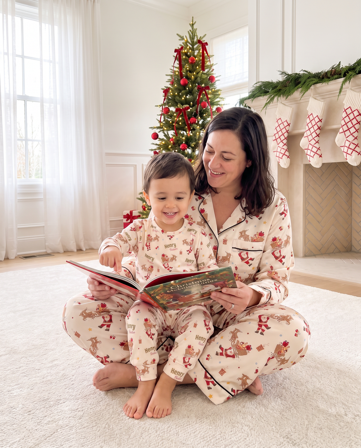 Mom in Santa's Joyride pajamas reading a Christmas book with her son on the rug