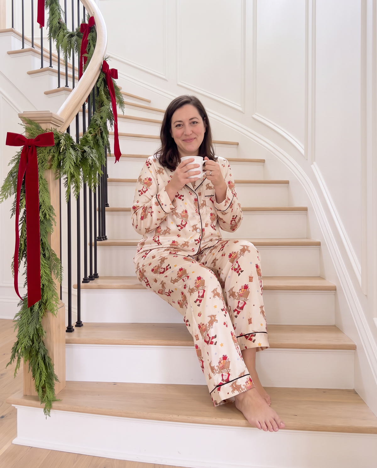 Woman in the Santa's Joyride long sleeve pajama set sitting on a garland staircase with cocoa