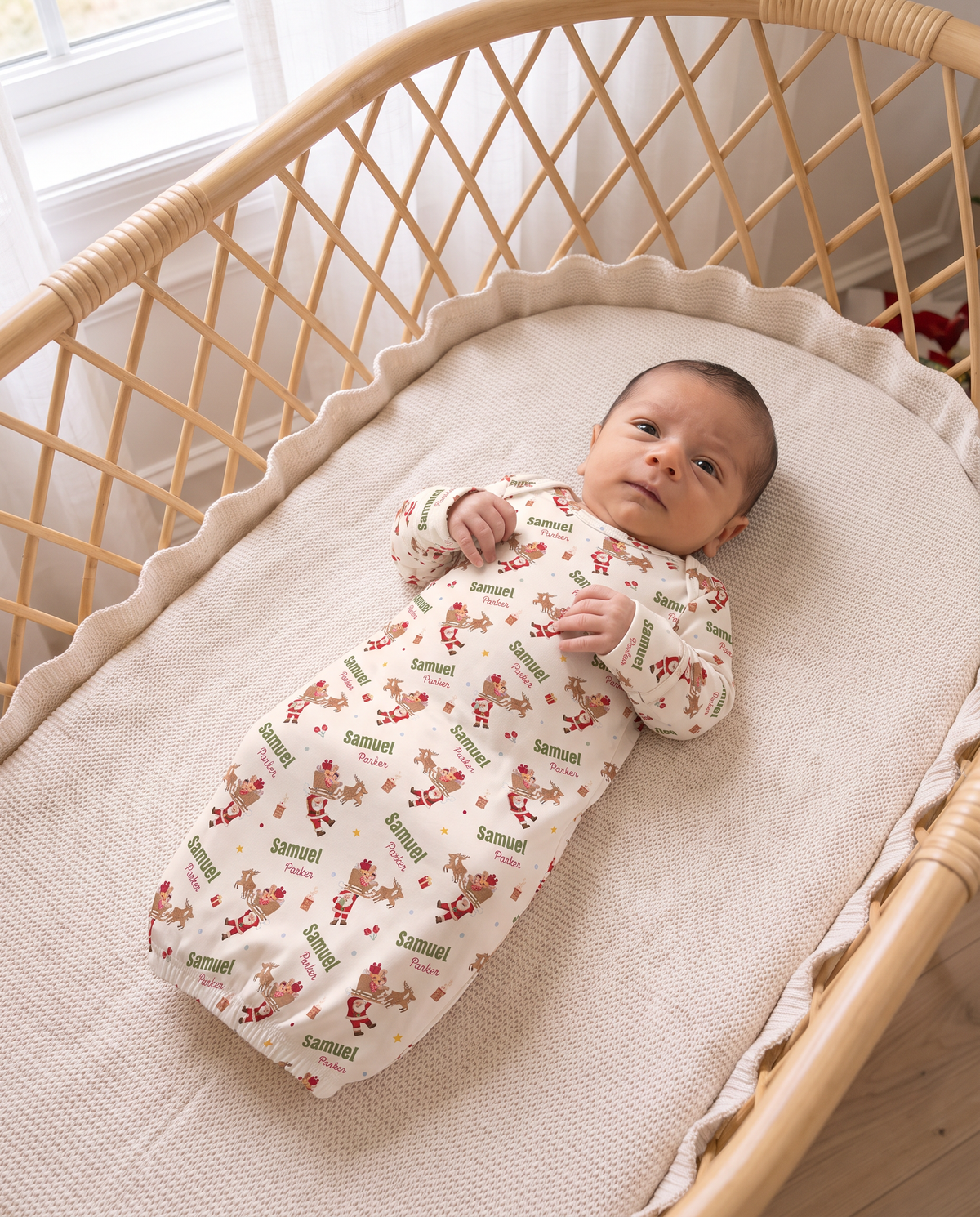 Baby in the personalized Santa's Joyride sleep gown, top view of a rattan bassinet
