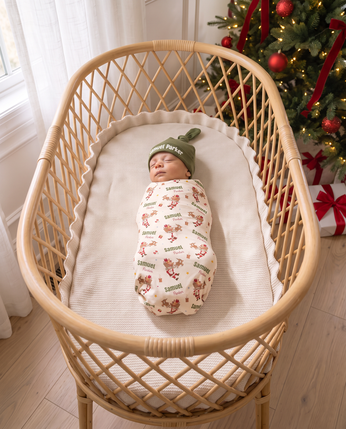 Swaddled newborn in Santa's Joyride print with knotted hat, top view of a rattan bassinet