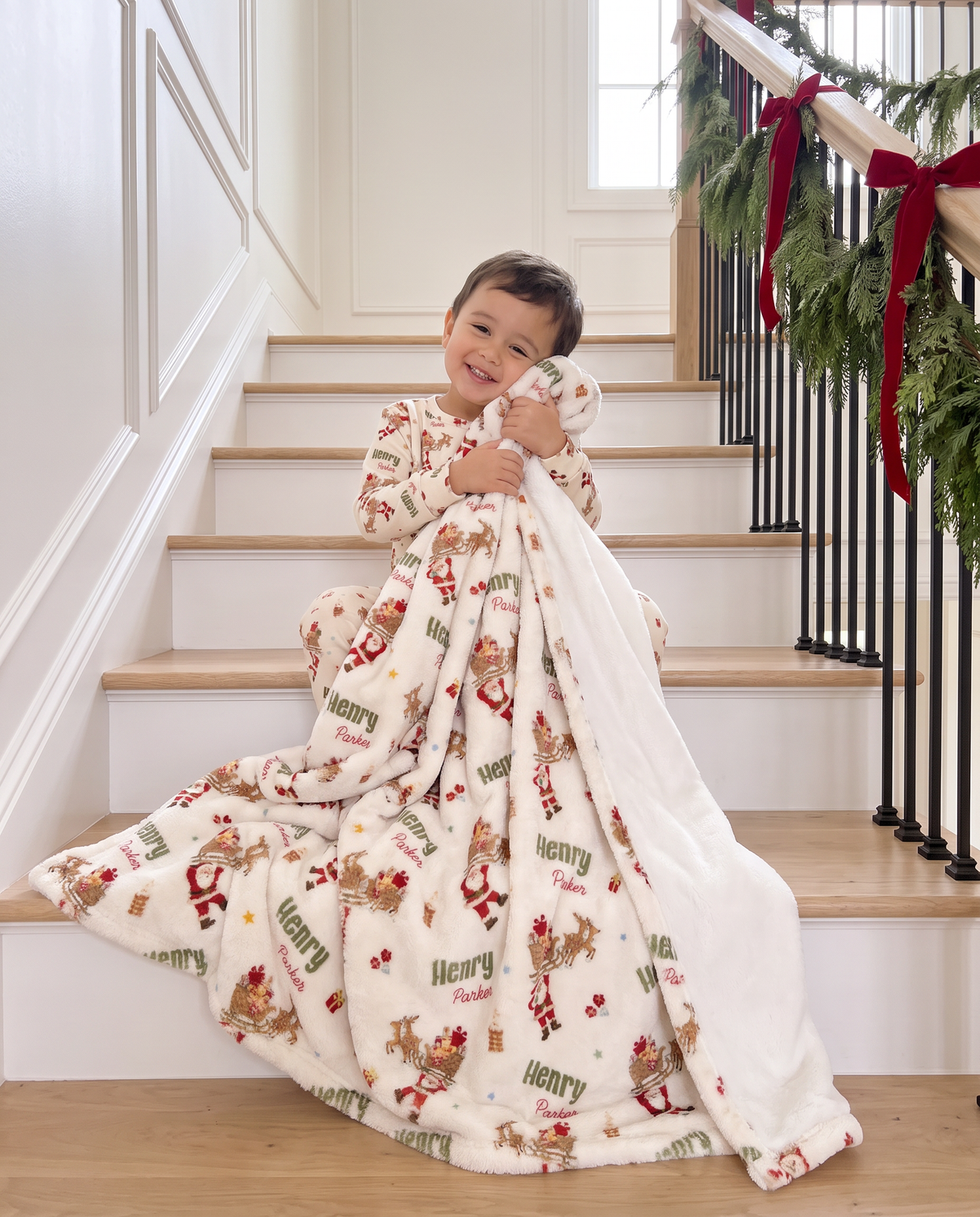 Toddler wrapped in a personalized Santa's Joyride blanket sitting on a garland-trimmed staircase