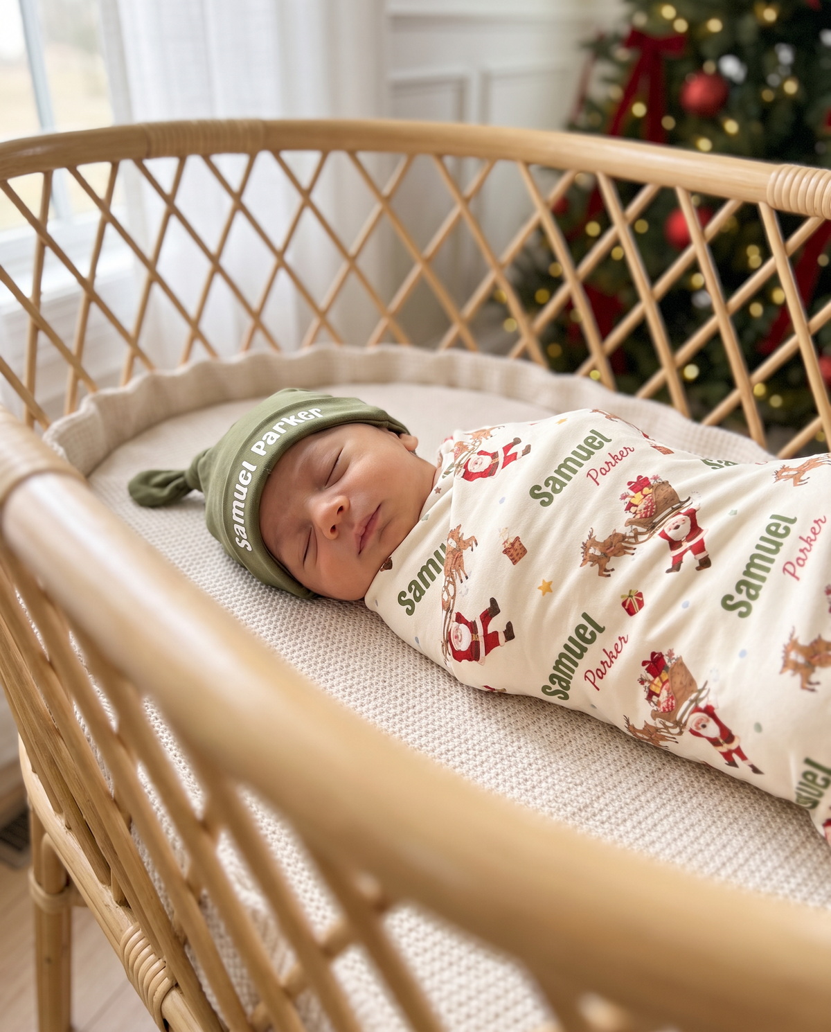 Close view of baby in the personalized Santa's Joyride swaddle and name knotted hat in a bassinet