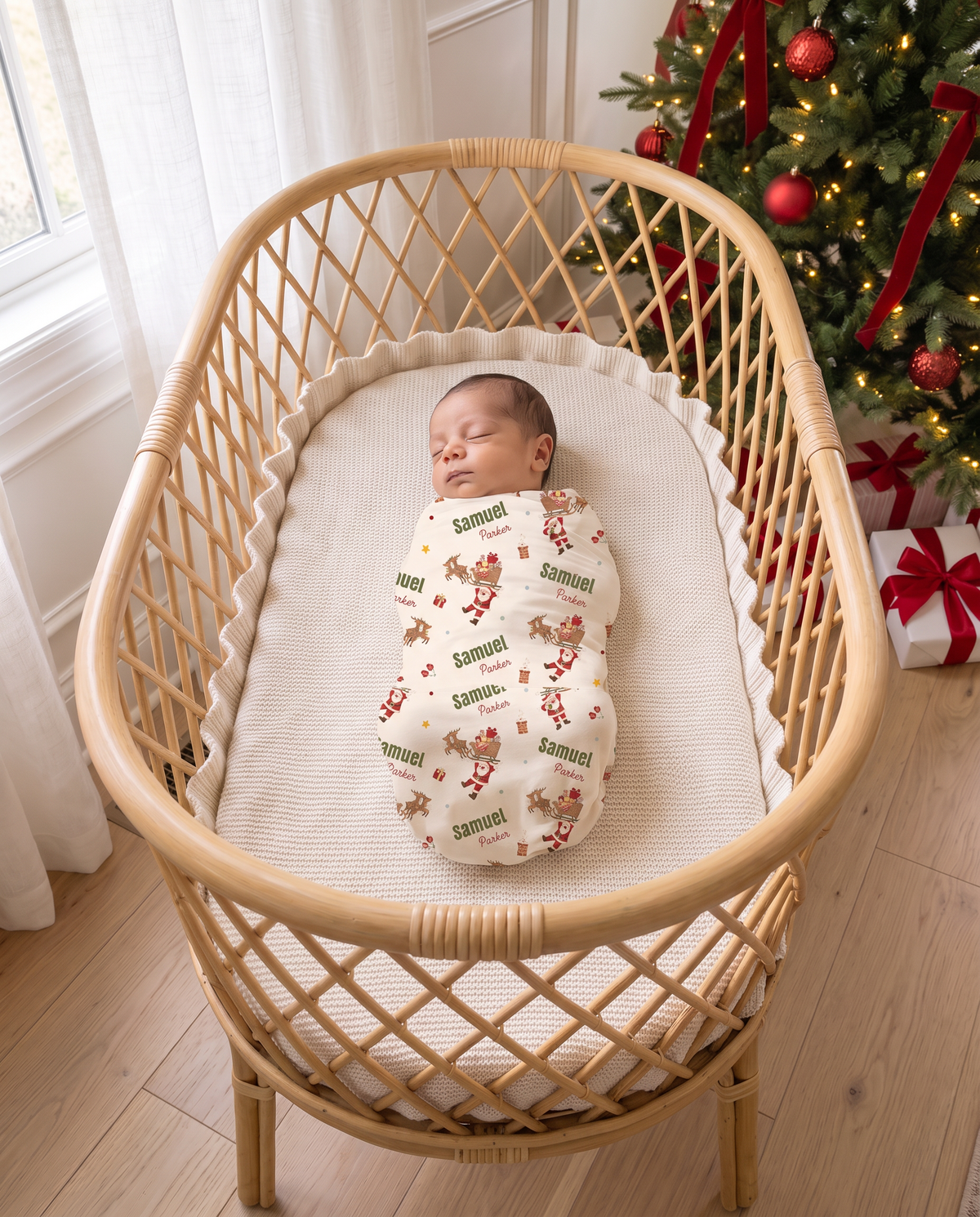 Baby swaddled in Santa's Joyride print in a rattan bassinet beside a decorated Christmas tree
