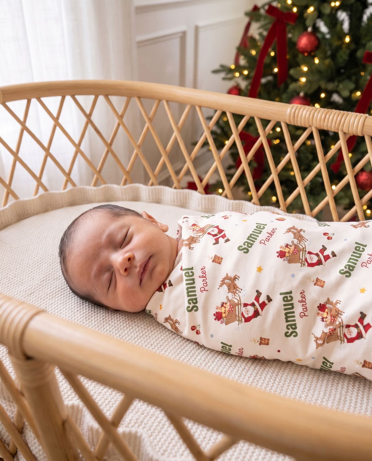 Sleeping newborn wrapped in the Santa's Joyride swaddle inside a rattan bassinet