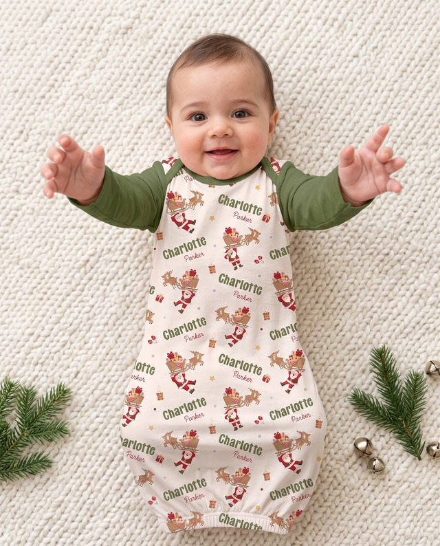 Baby reaching up in Santa's Joyride sleep gown with olive sleeves, on a cream blanket with pine sprigs