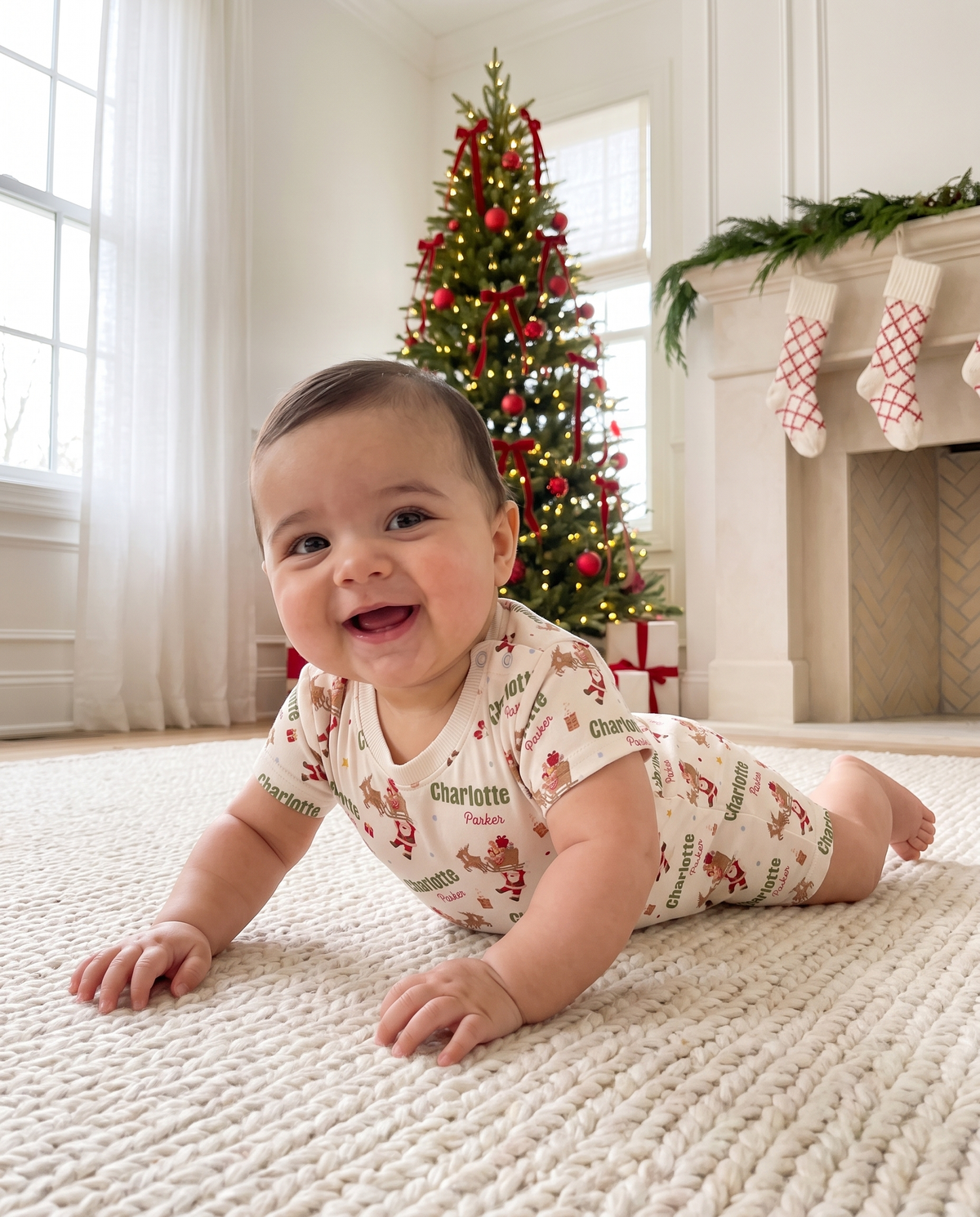 Baby in Santa's Joyride short-sleeve romper on the rug in front of a decorated Christmas tree