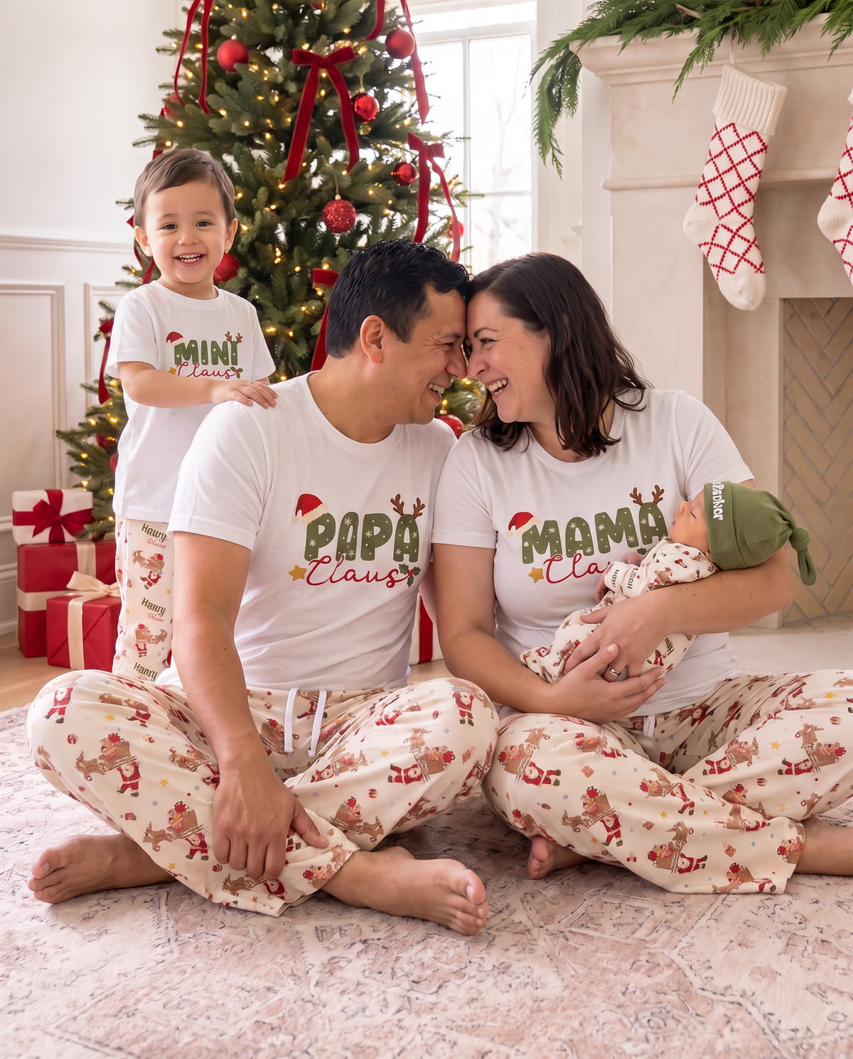 Family in Claus graphic tees and Santa's Joyride pants on the rug by the tree