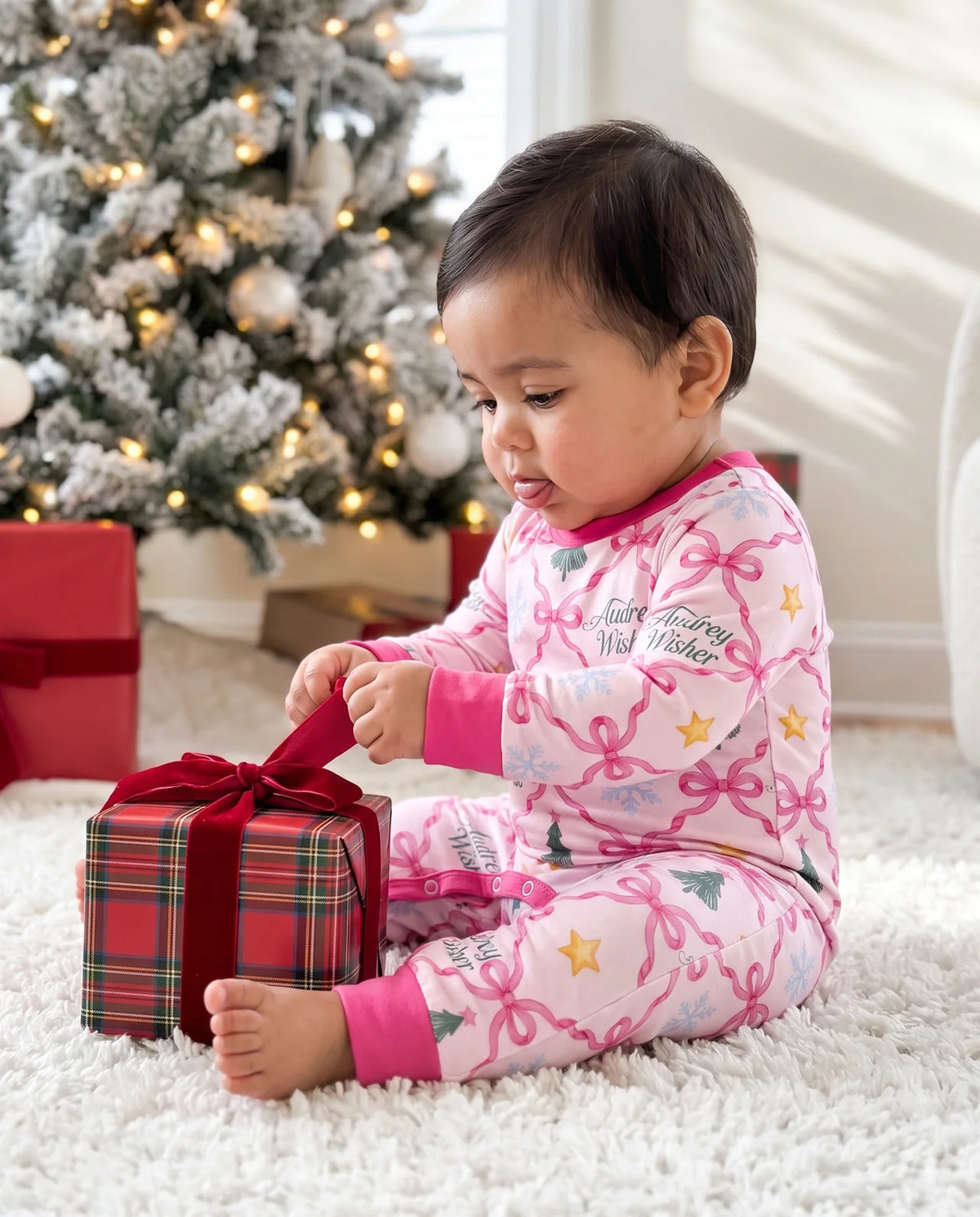 A baby pulling the ribbon on a single wrapped gift beside the Christmas tree