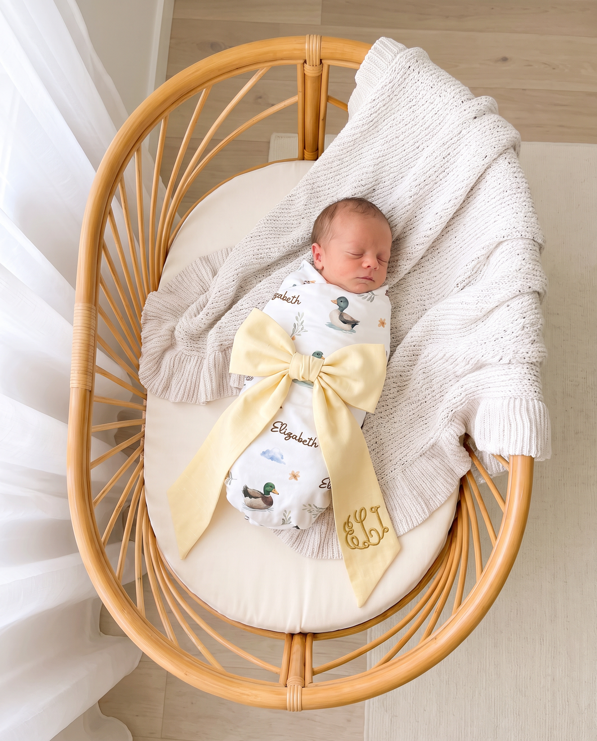 Newborn in a bassinet wearing the light yellow bow sash