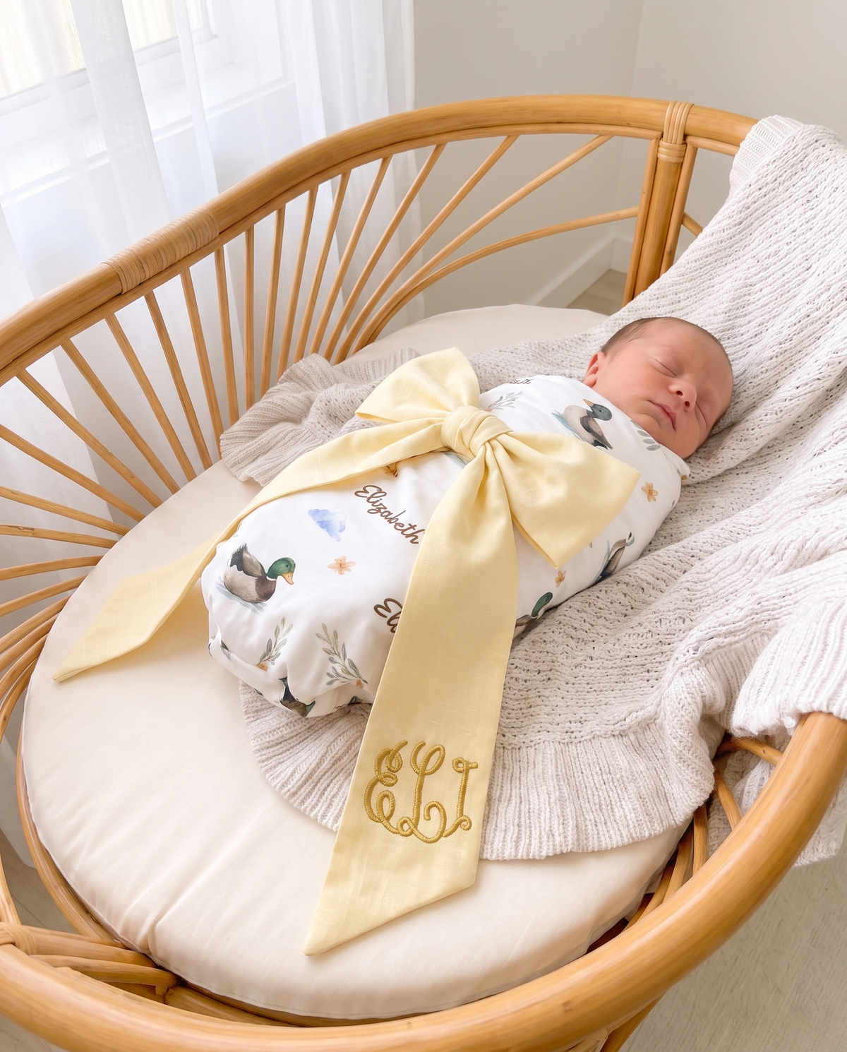 Light yellow bow sash draped over a swaddled baby in a rattan crib