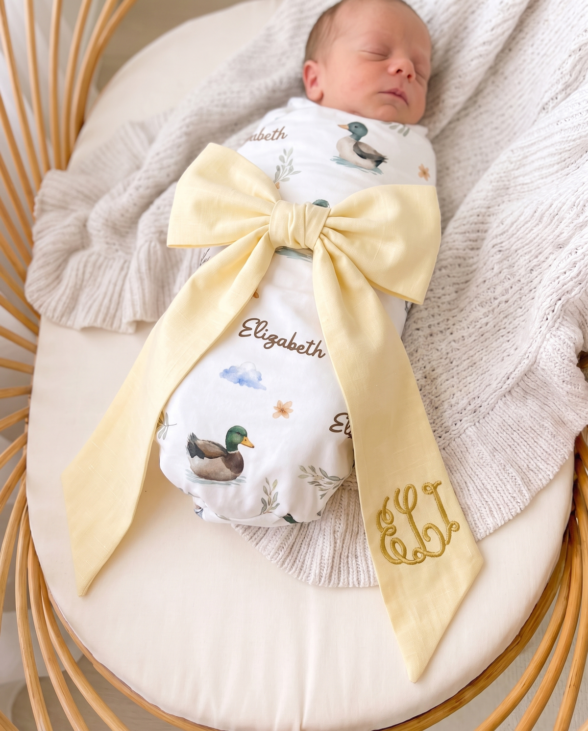 Close-up of the light yellow bow sash with embroidered monogram on a newborn