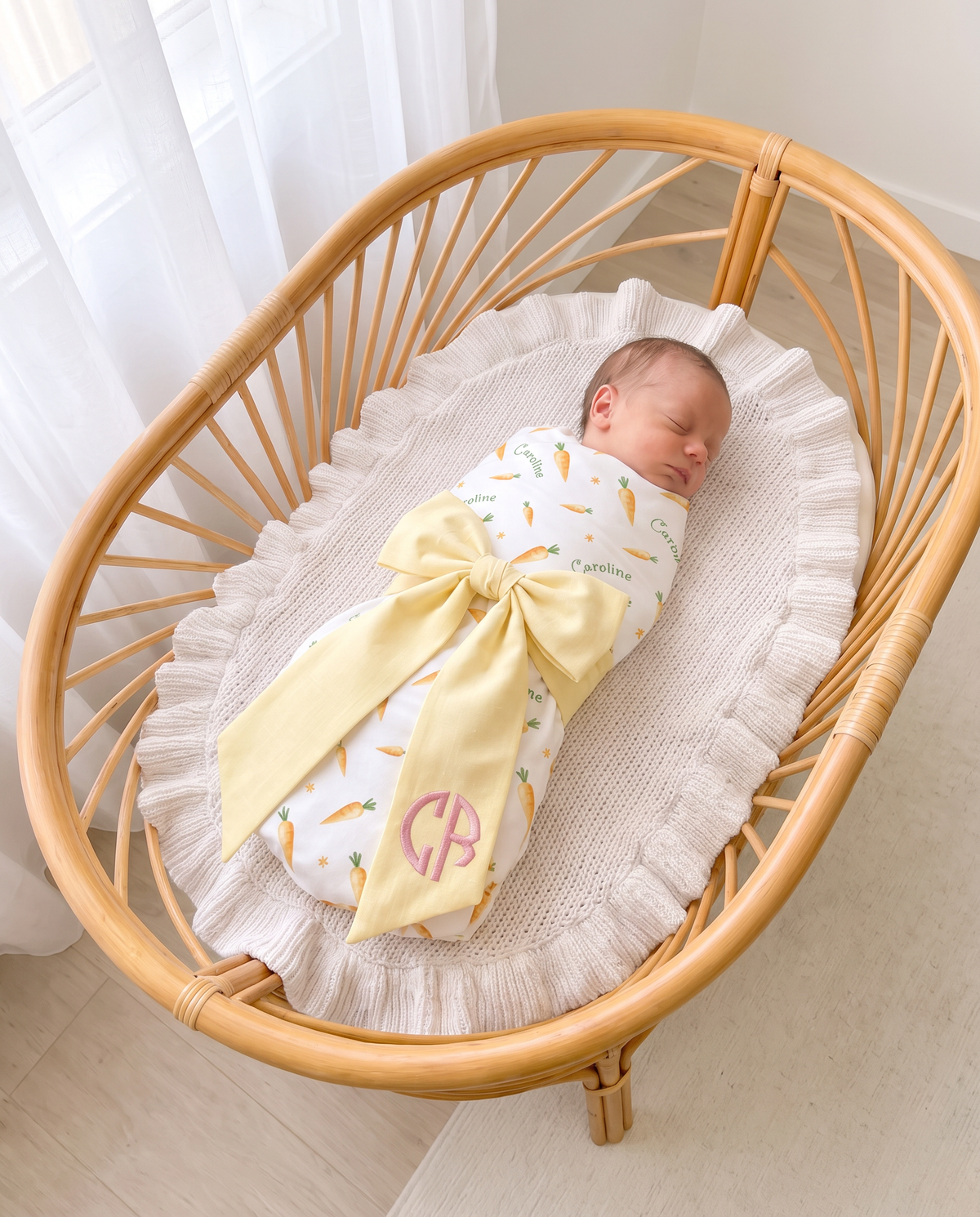 Light yellow bow sash with pink monogram on a swaddled newborn in a bassinet