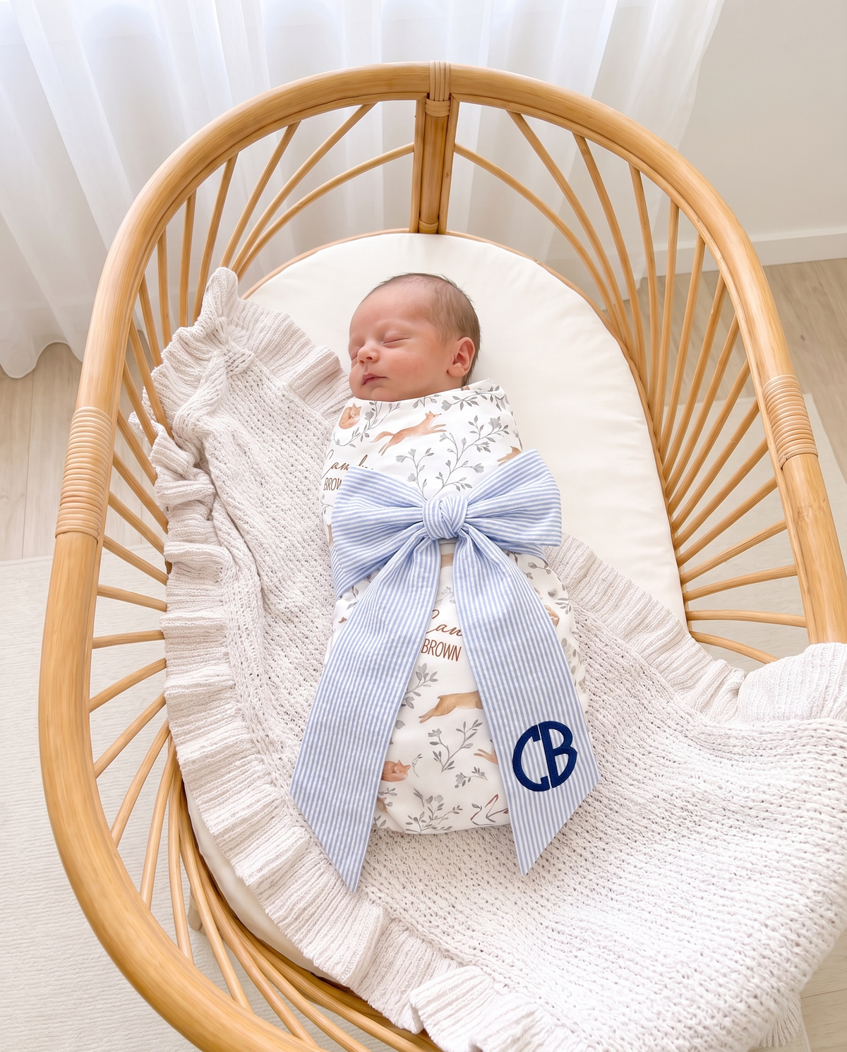 Personalized Newborn Bow Sash in Striped Blue on a swaddled newborn in a rattan bassinet