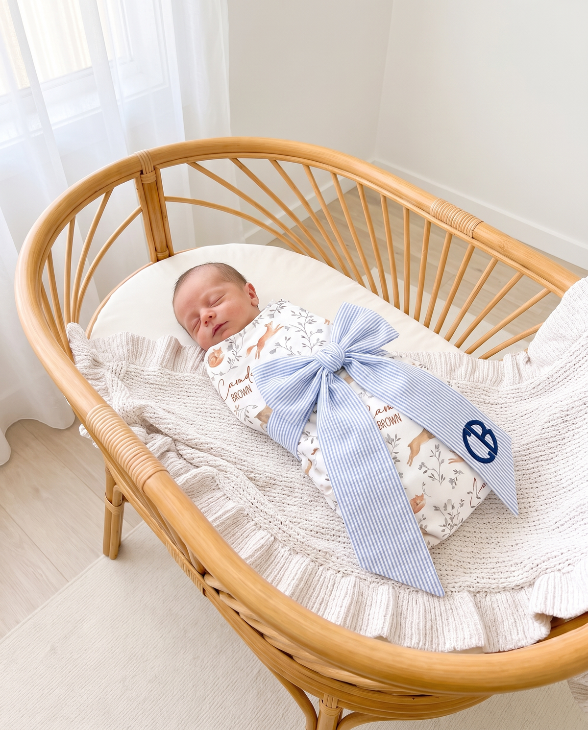 Newborn in a bassinet wearing the striped blue bow sash