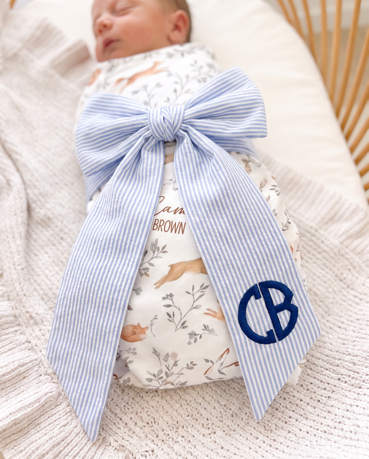 Close-up of the striped blue bow sash with navy embroidered monogram on a newborn