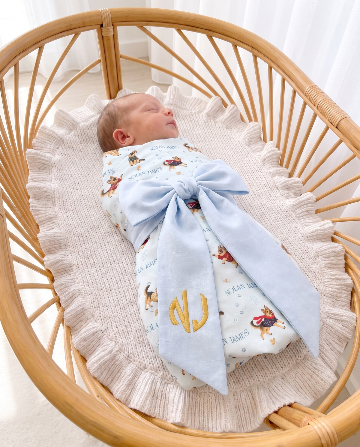 Swaddled baby with the light blue bow sash laid across in a rattan bassinet