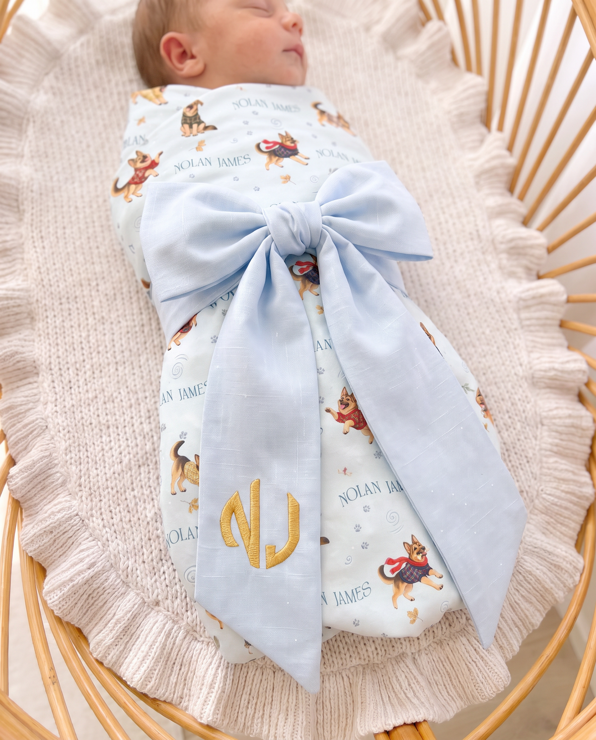 Close view of the light blue bow sash with gold monogram on a swaddled newborn