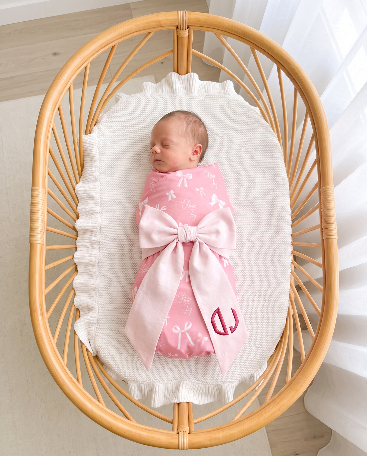 Baby swaddled in Pink Coquette print with the light pink bow sash in a rattan bassinet