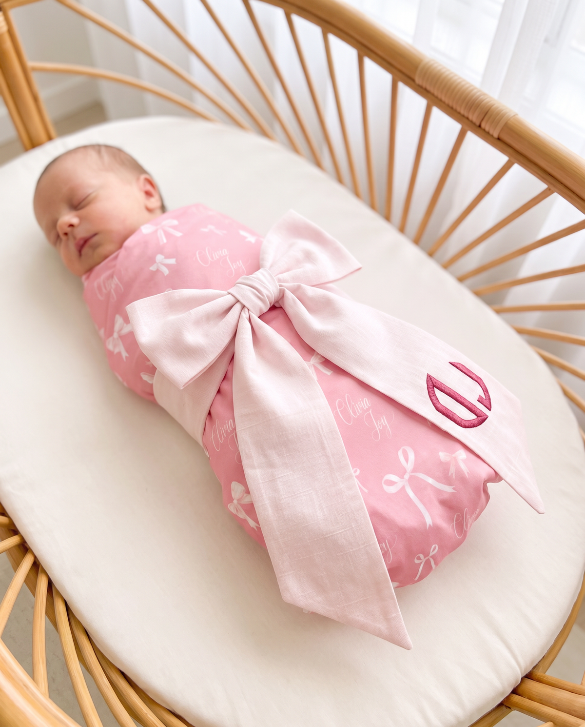 Sleeping newborn with the light pink bow sash and pink monogram in a bassinet