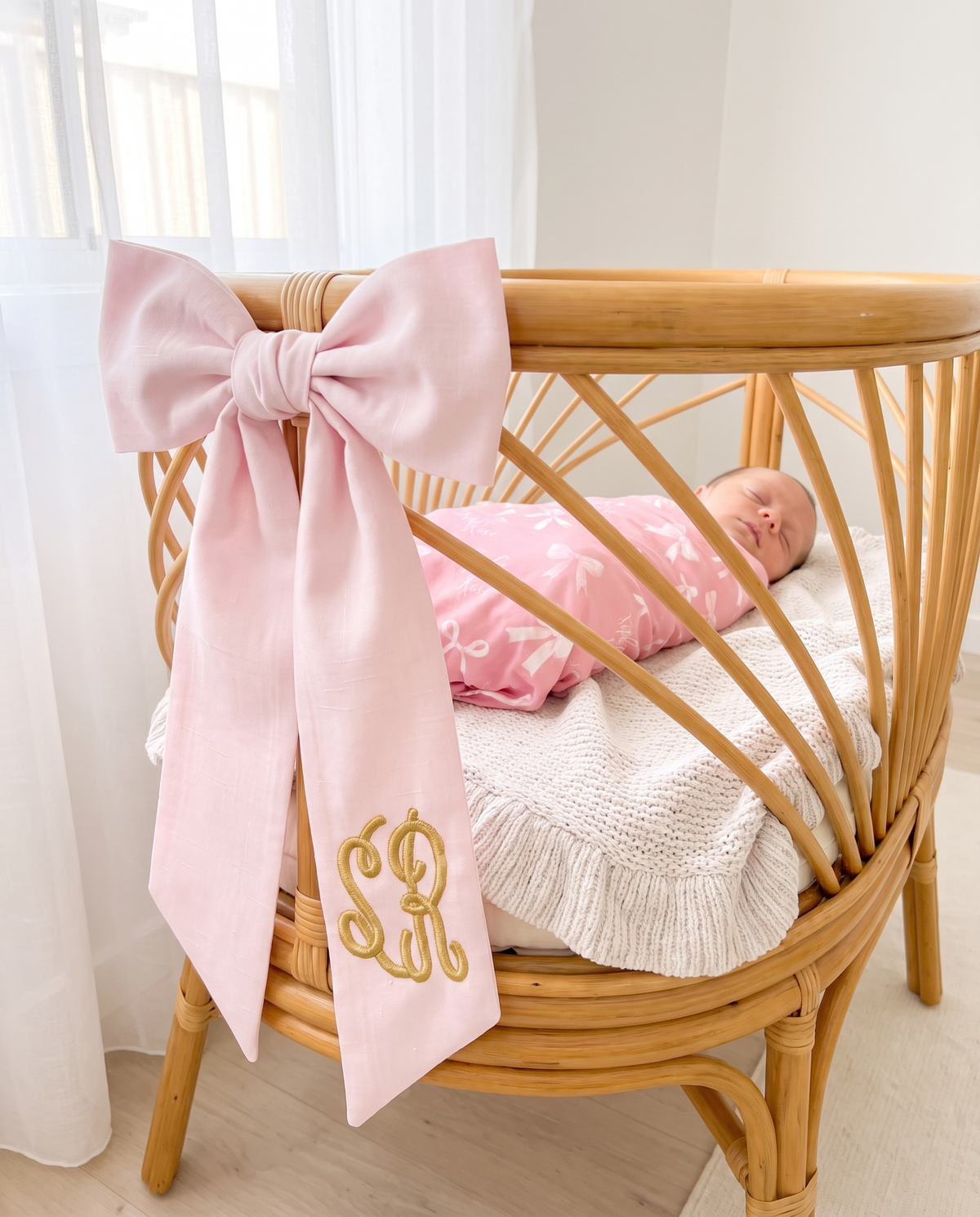 Light pink bow sash tied on a rattan bassinet rail as nursery decor