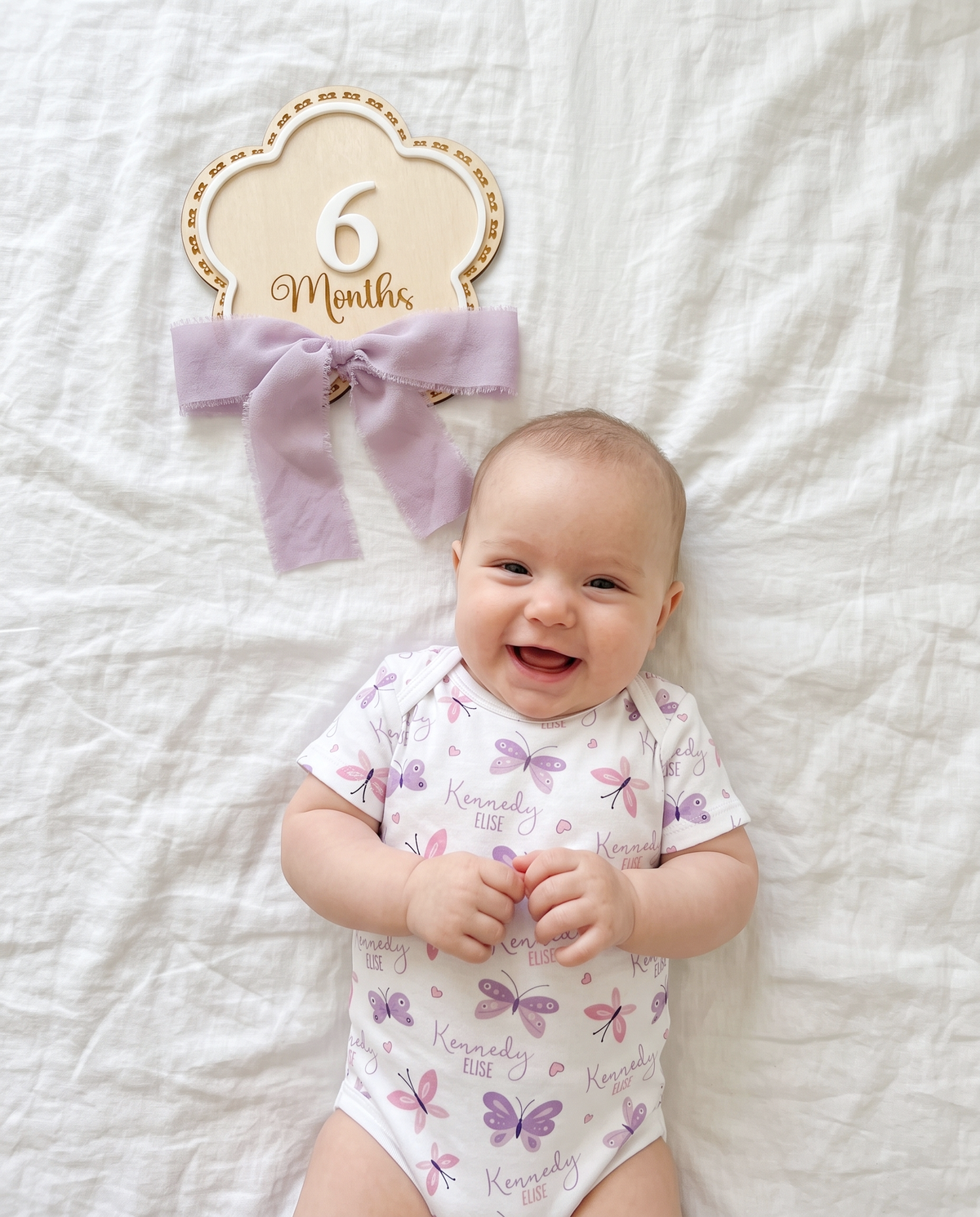 Flowers monthly milestone wood sign set to 6 Months resting beside a baby in a floral bodysuit