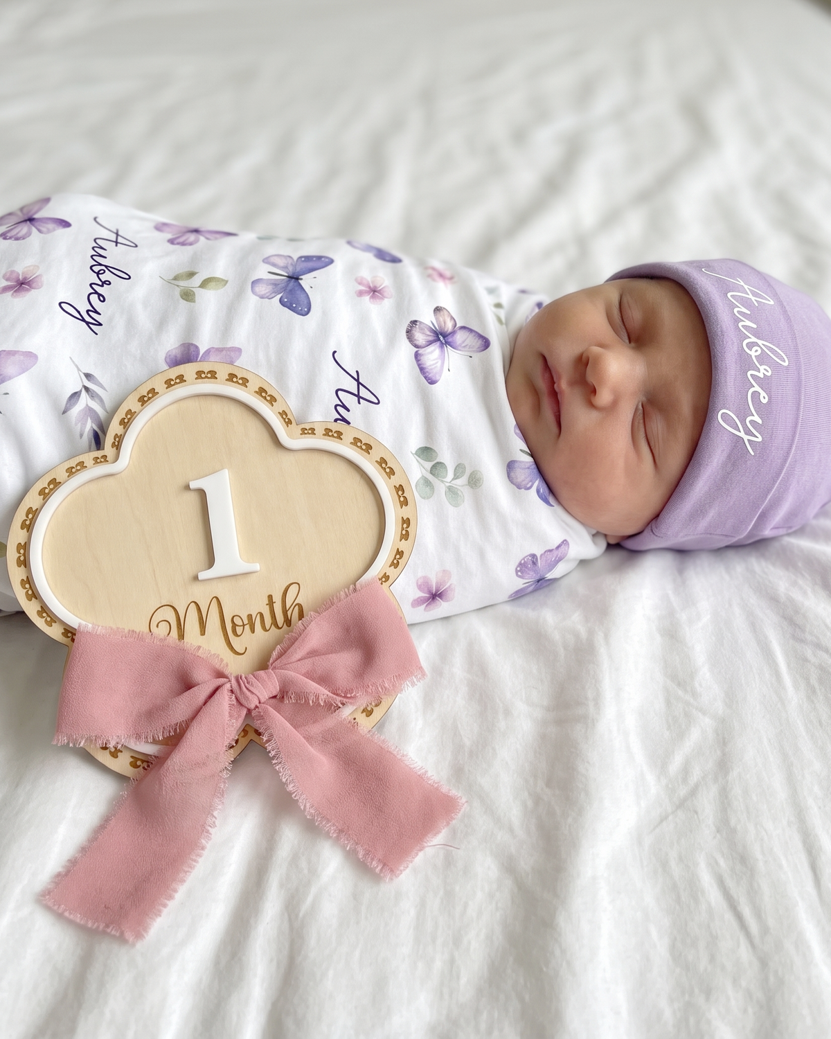 Flowers monthly milestone wood sign photographed low beside a baby on white bedding