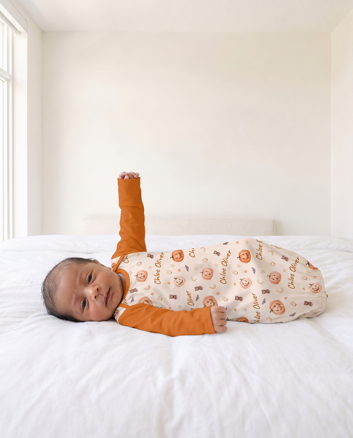 Side profile of baby raising one solid orange sleeve of the Golden Jack sleep gown