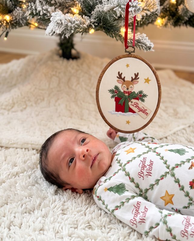 Baby lying on a cozy rug under an embroidered North Trail sign