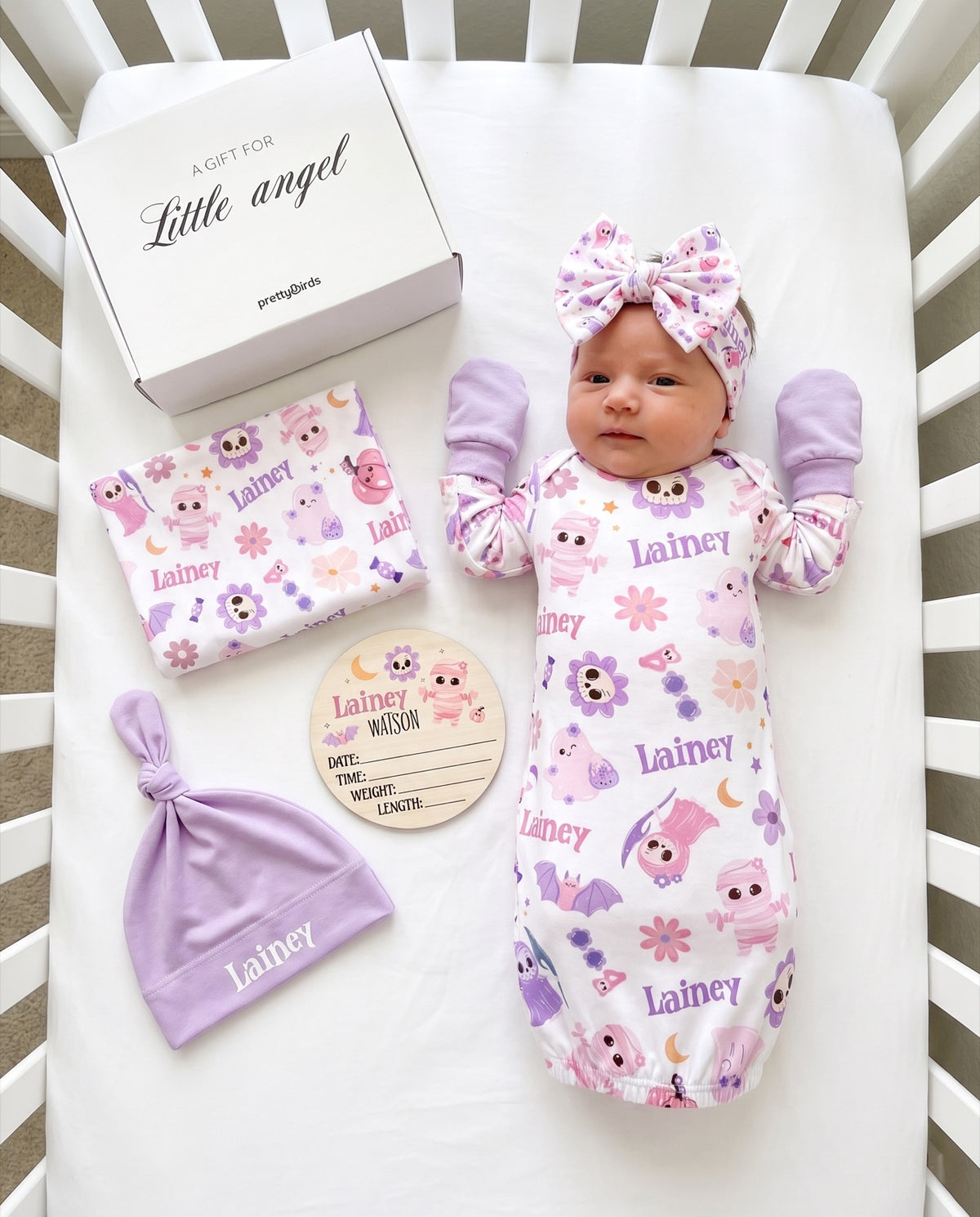 Blush Boo Halloween baby gift box with swaddle, gown, hat, headband, mittens and wood sign in a crib, personalized with the name Lainey