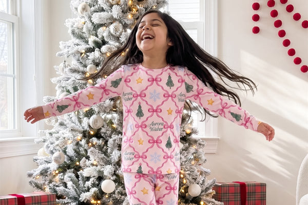 Girl twirling in pink North Star Christmas pajamas beside a frosted Christmas tree