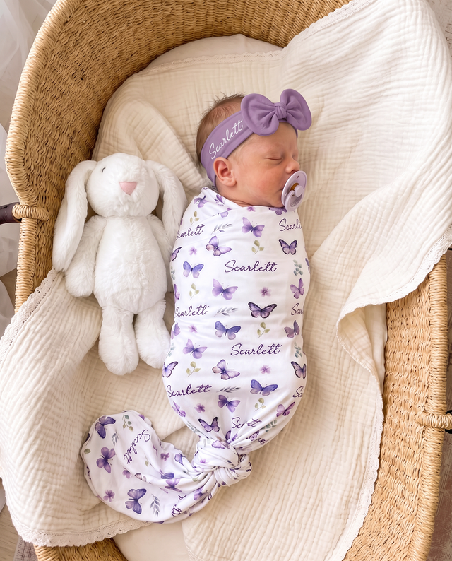 Newborn swaddled in the personalized purple butterfly swaddle with a matching bow headband, beside a plush bunny