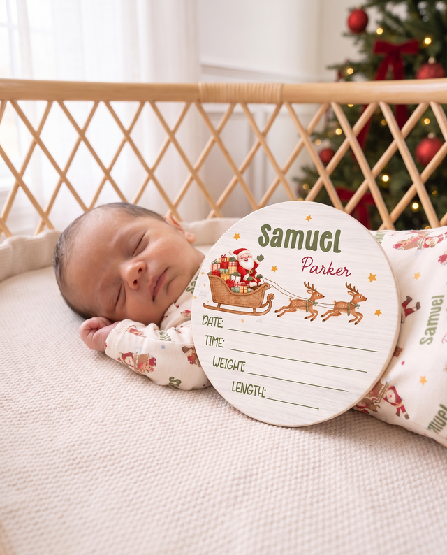 Newborn sleeping next to the Santa's Joyride birth stats sign in a rattan bassinet