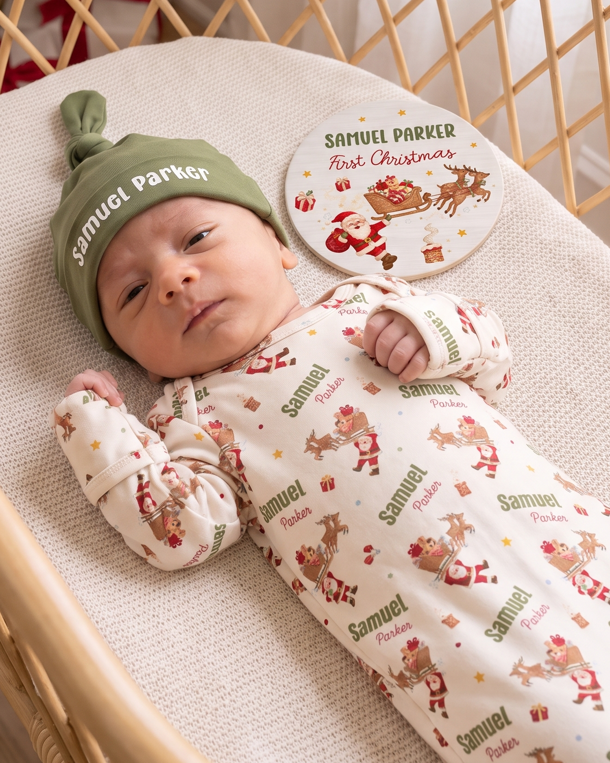 Baby in a knotted hat lying next to the Santa's Joyride First Christmas name sign