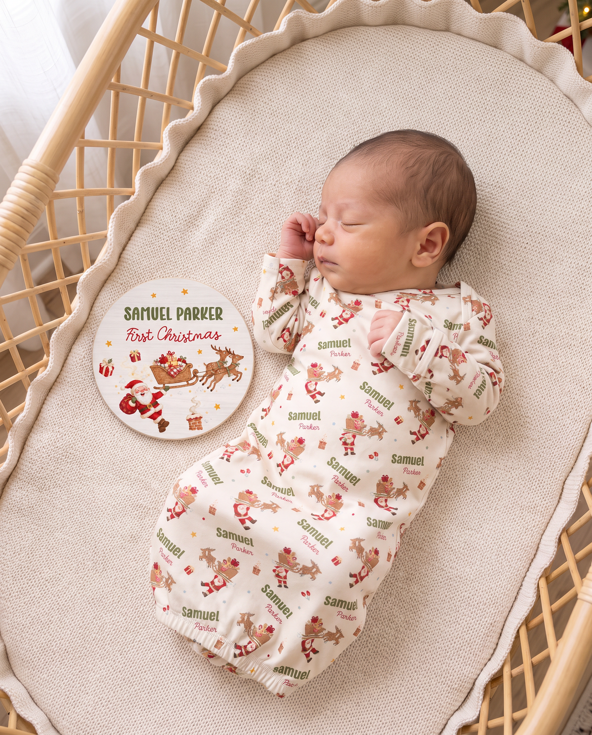 Newborn in the Santa's Joyride sleep gown beside the personalized name sign in a bassinet