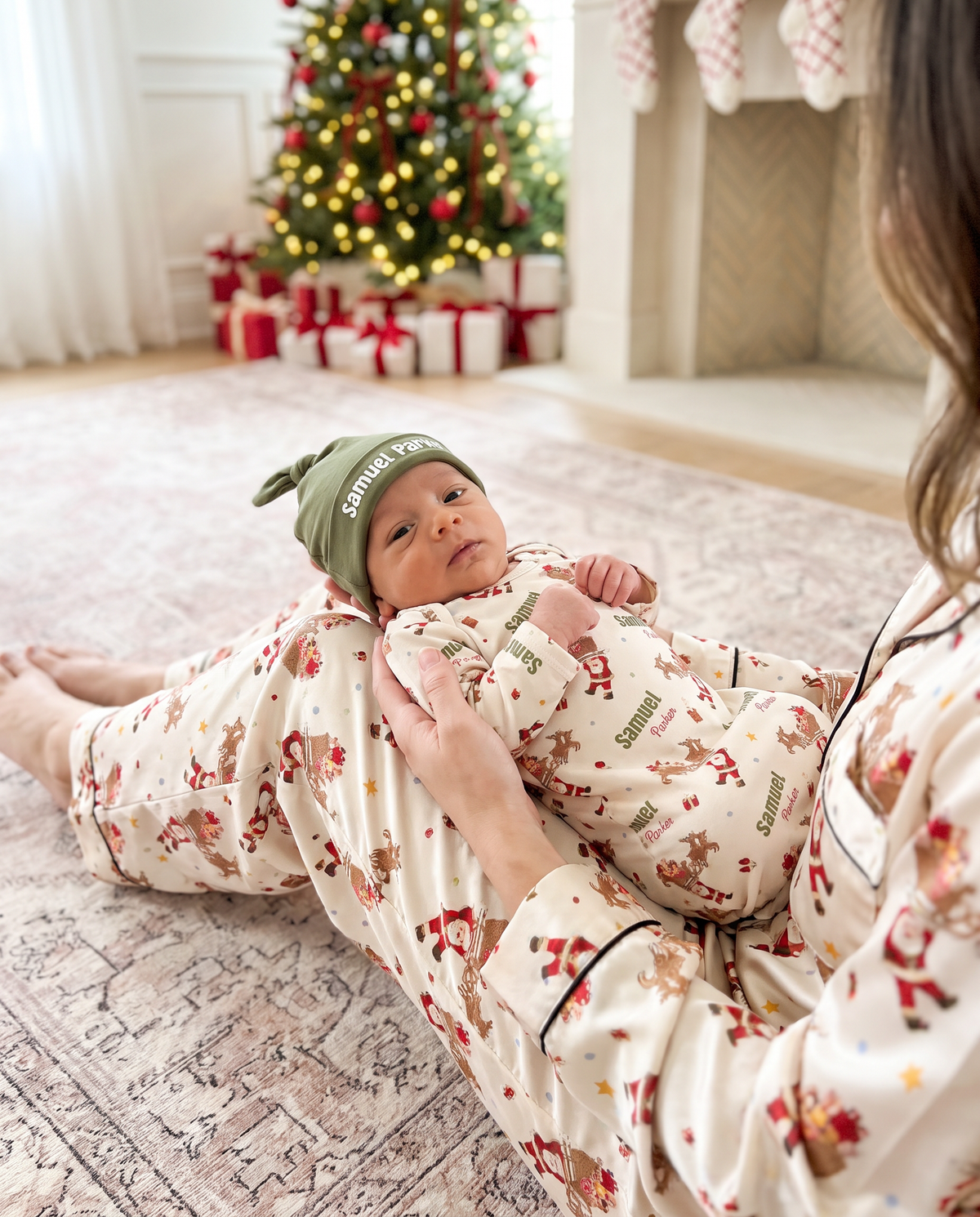 Mom lying beside her newborn in the Santa's Joyride sleep gown near the Christmas tree