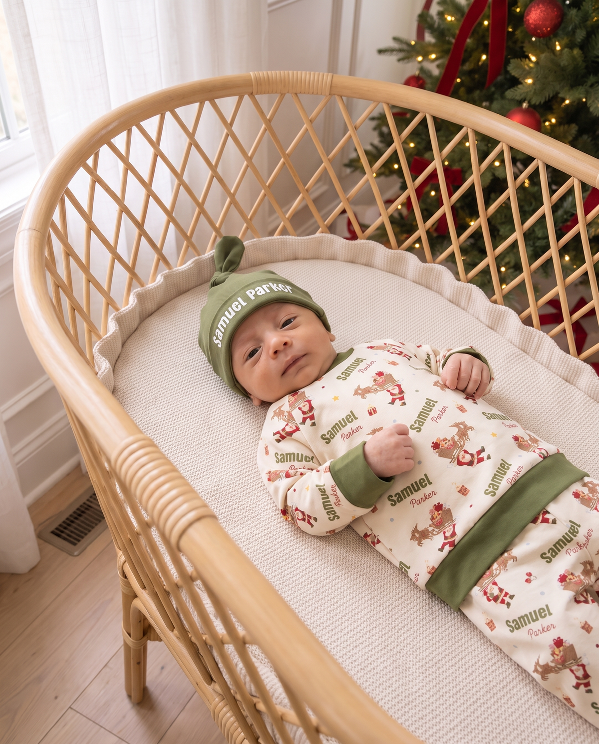 Newborn in the personalized Santa's Joyride pajama set and knotted hat in a rattan bassinet