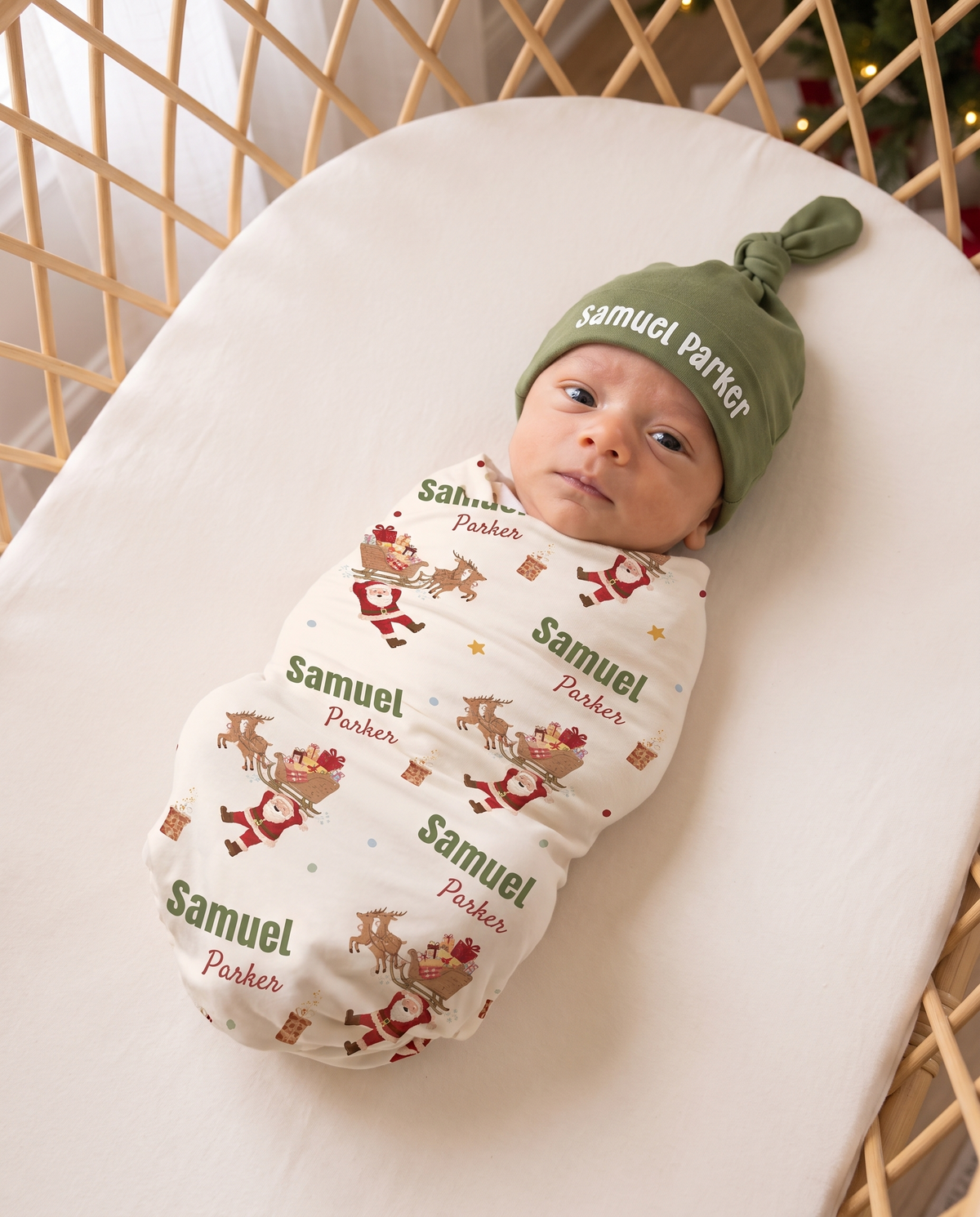 Newborn in the personalized Santa's Joyride swaddle and olive knotted hat, close view from above