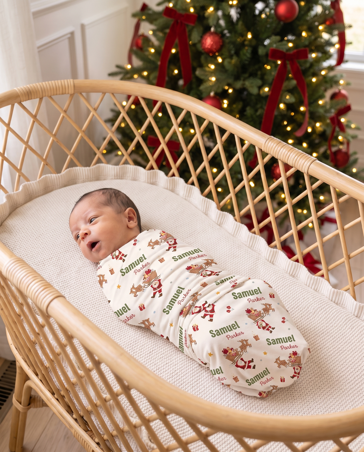 Newborn in the Santa's Joyride swaddle yawning in a rattan bassinet near the Christmas tree