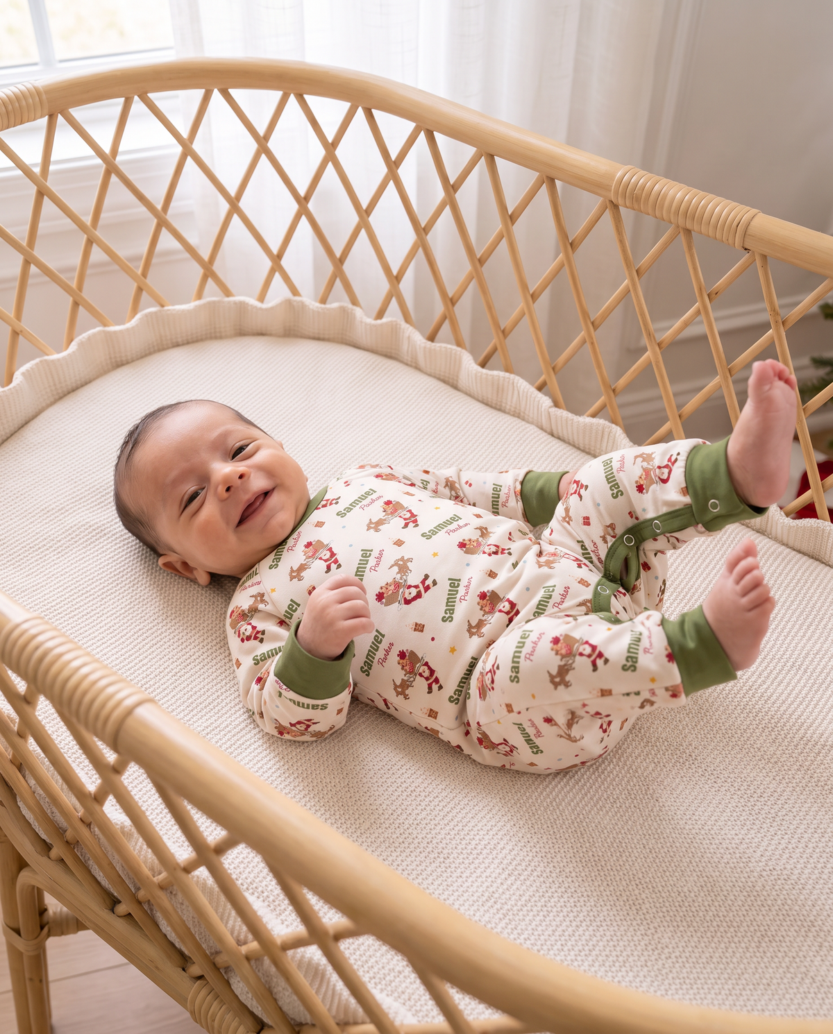 Smiling baby wearing Santa's Joyride long-sleeved romper in a rattan bassinet